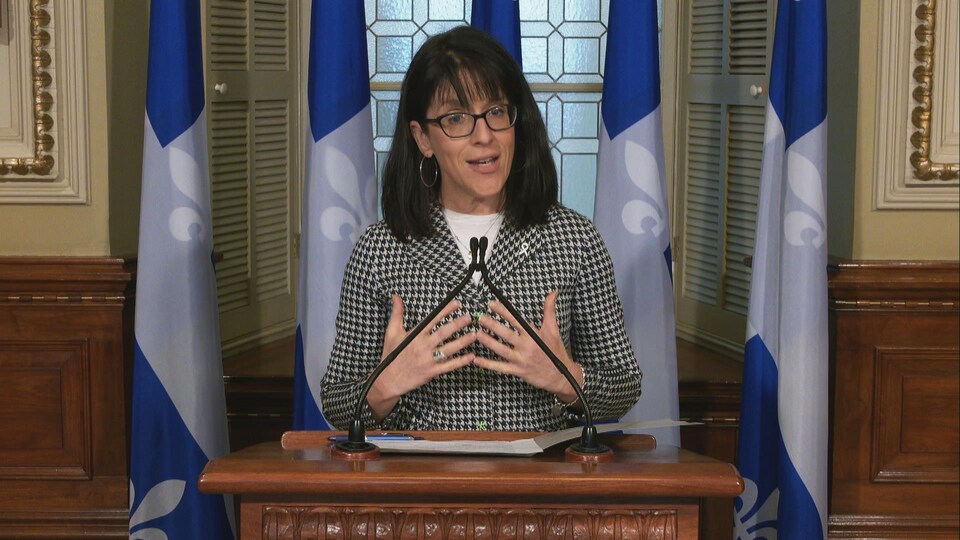 Sonia LeBel donne un point de presse à l’Assemblée nationale. Elle se tient debout, derrière un lutrin et devant des drapeaux du Québec.