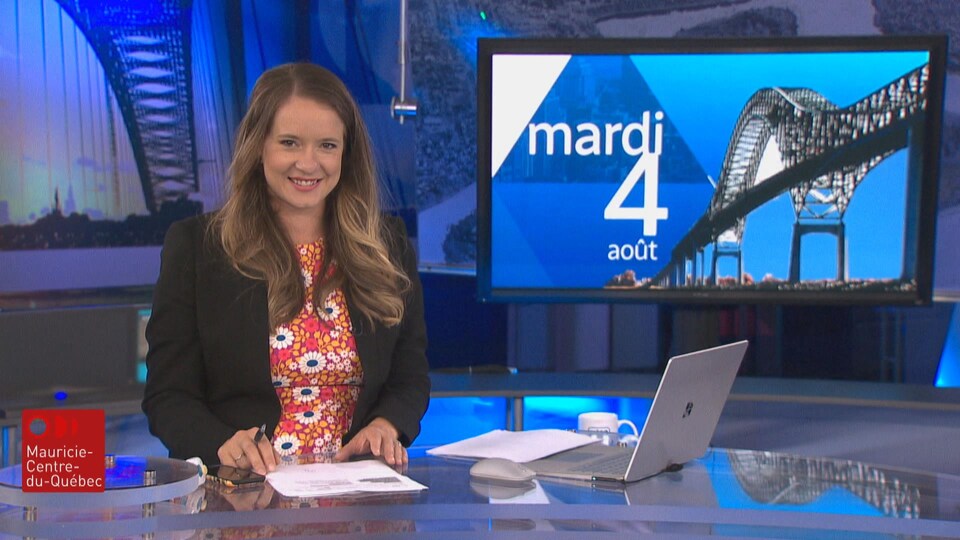 Sophie Bernier à son bureau, debout, avec un ordinateur et des feuilles ainsi qu'un écran qui dit : mardi 4 août.