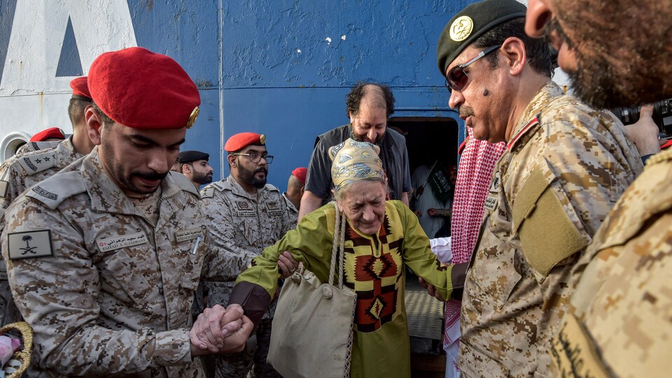 Des soldats tiennent une dame âgée par la main.