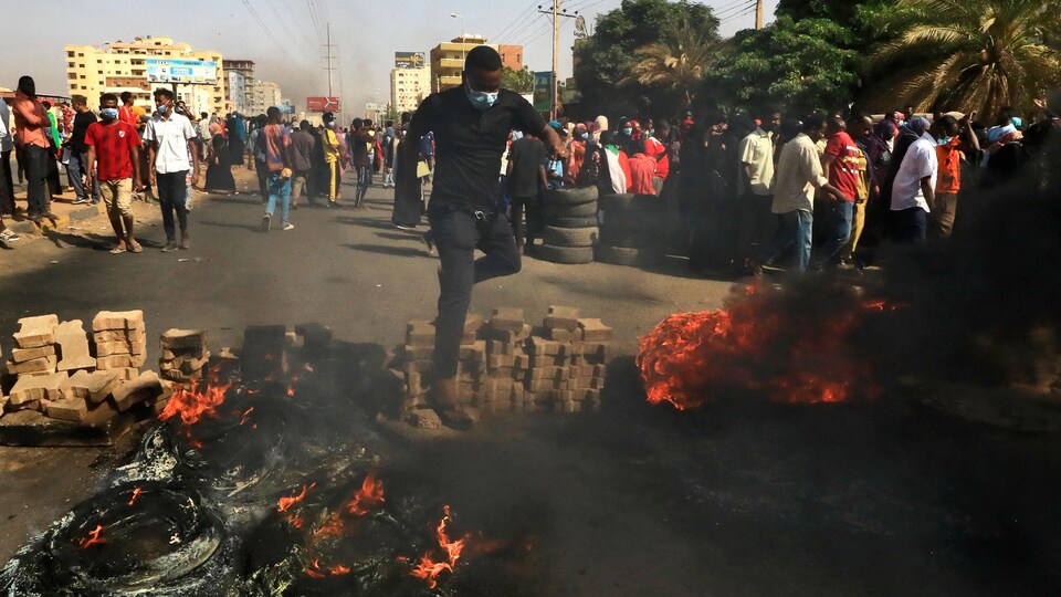 Un homme saute par-dessus des pneus en feu. Une foule se trouve derrière lui.