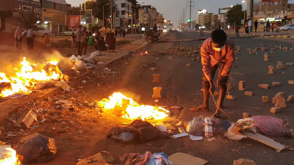 Un manifestant au milieu d'une rue en feu de Khartoum jonchée de briques.