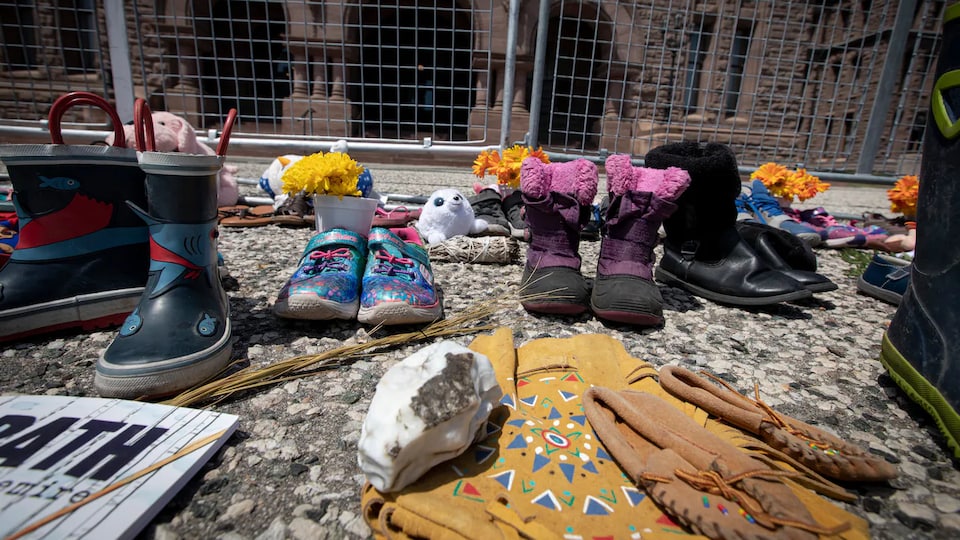 Des souliers d'enfants et d'autres objets déposés à Queen's Park à la mémoire des élèves morts au pensionnat pour Autochtones de Kamloops.