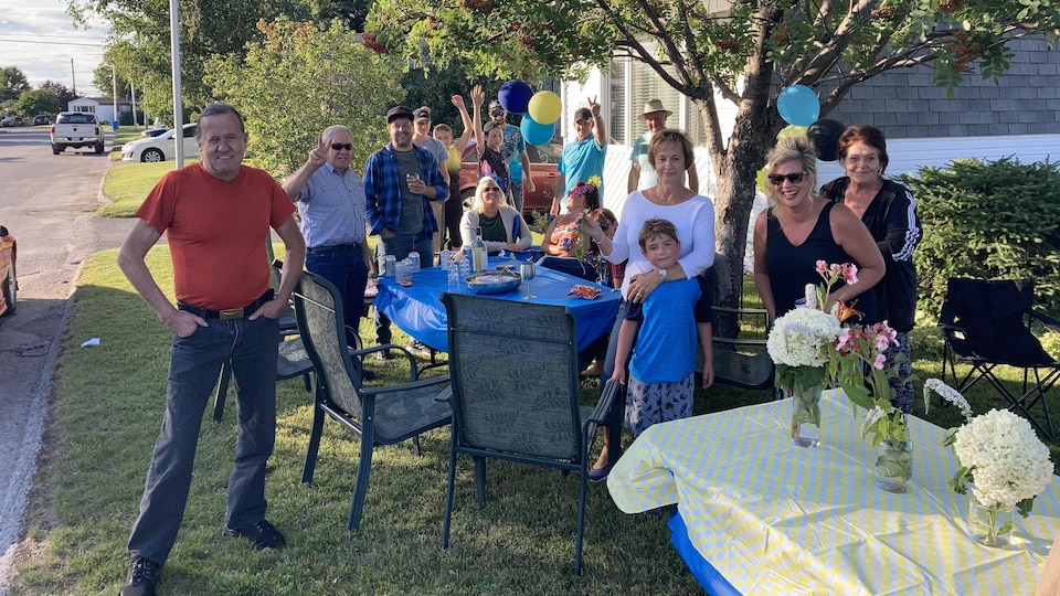 Des membres de deux familles réunies sur leur parterre avec des tables pour prendre un repas.