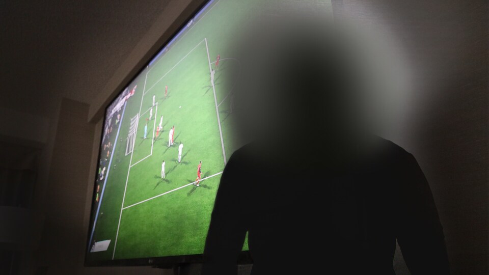 Un homme dont le visage est caché pose devant un écran de télévision.