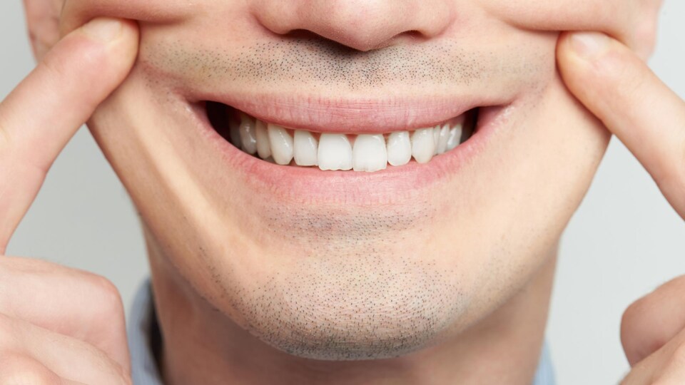 Un homme fait un faux sourire avec les dents et les doigts en gros plan.