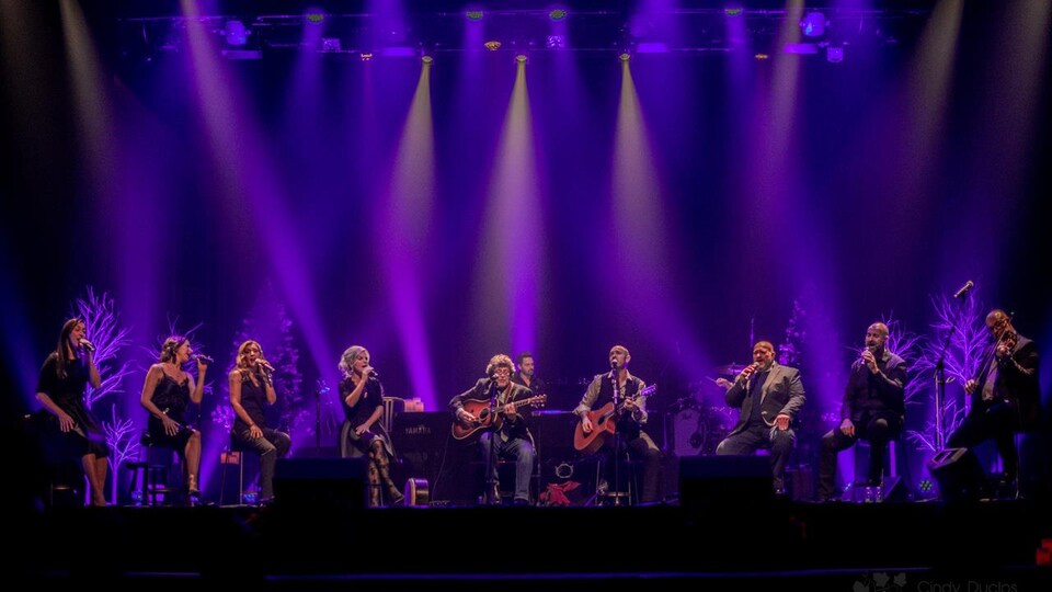 Les neuf artistes chantent et jouent de la guitare et du violon sur scène.