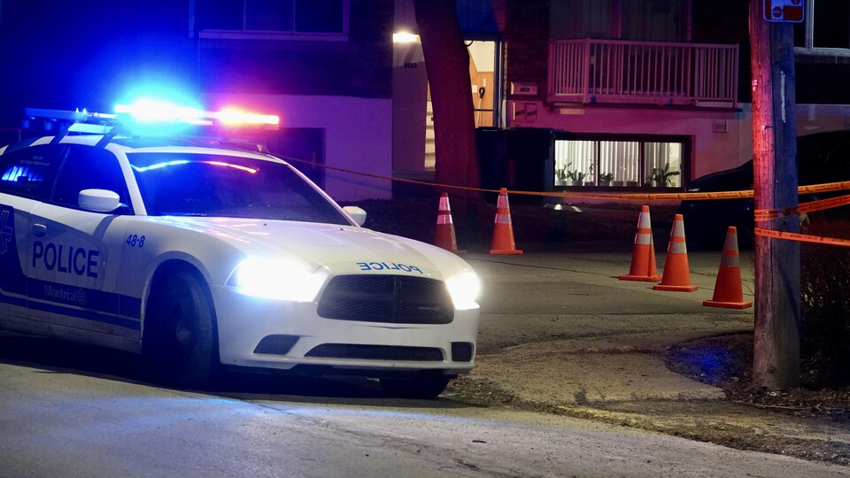 Une voiture de police, le soir, devant un immeuble avec périmètre de sécurité.