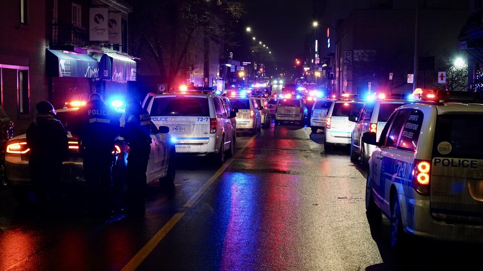 De très nombreux véhicules de police sont au milieu d'une rue du centre-ville de Montréal, leurs gyrophares en fonction.
