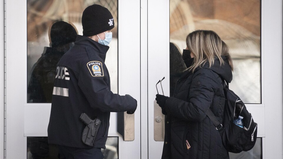 Un policier discute avec une dame devant une porte vitrée en hiver. 