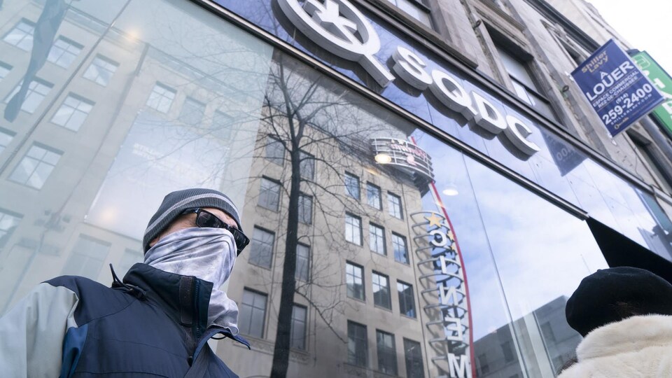 Un homme ayant remonté son chandail pour se cacher le visage attend devant une succursale de la Société québécoise du cannabis.
