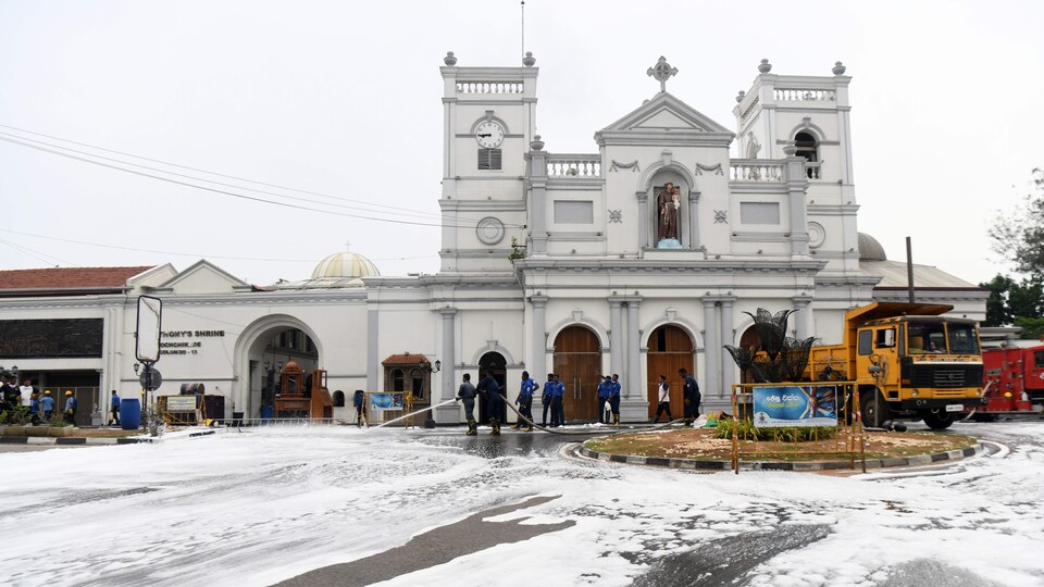 Devant une église, des gens tiennent des lances à eau pour nettoyer les alentours.