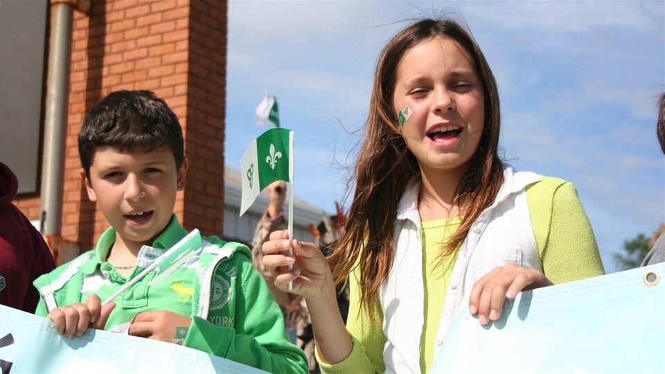 Deux enfants brandissent le drapeau franco-ontarien à la Saint-Jean-Baptiste dans le Grand Sudbury.