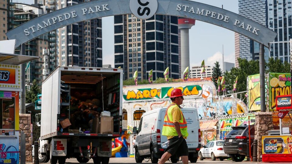Un travailleur marche sur le site du Stampede. Derrière lui, on voit des camions et des kiosques en voie d'installation pour le festival.
