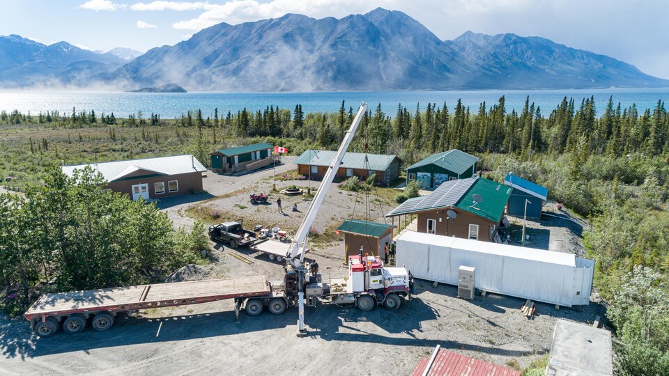 La station de recherche et la ferme en construction avec, en arrière-plan, un plan d'eau et des montagnes.
