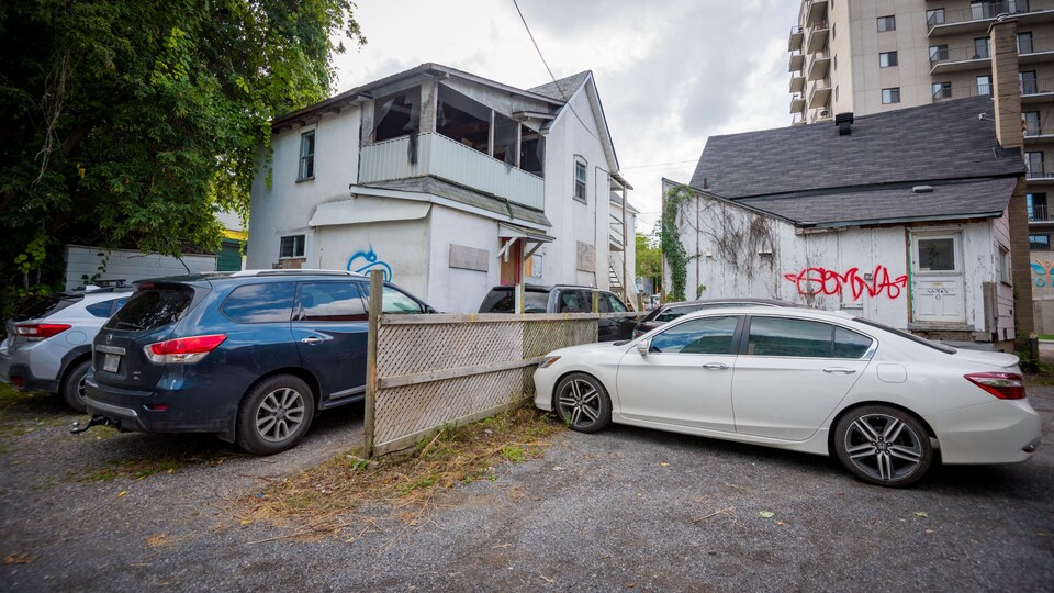 Cinq voitures sont garées devant deux taudis.