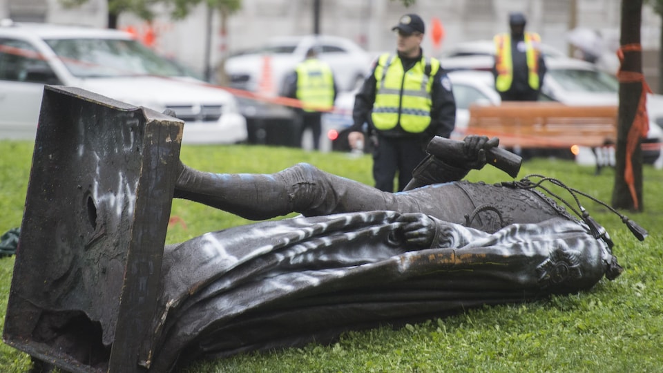 Des policiers montent la garde à côté de la statue, couchée de tout son long.