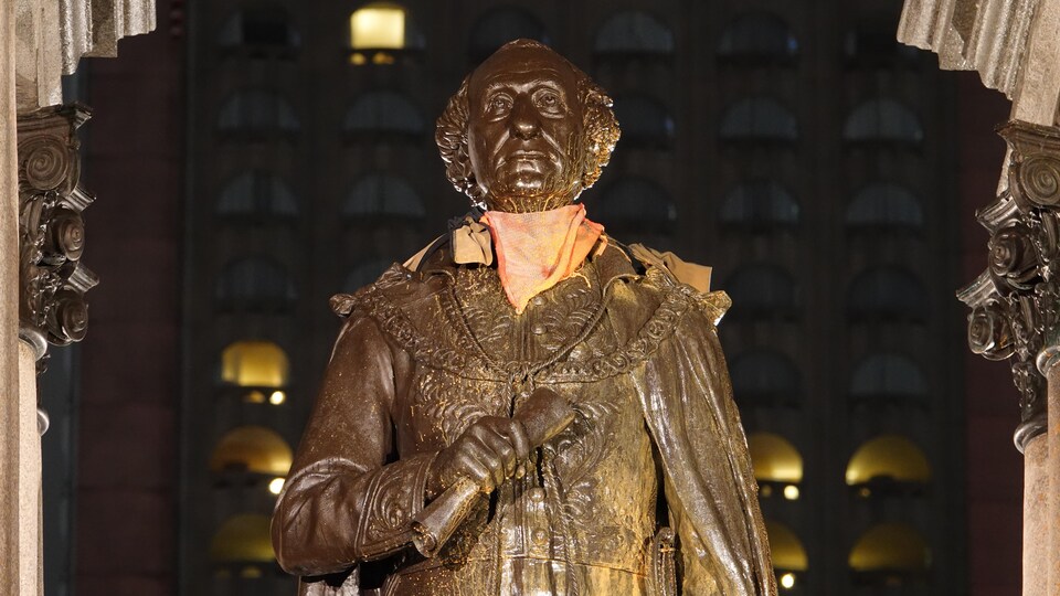 La statue d'un homme, photographiée le soir, est couverte de peinture orange.