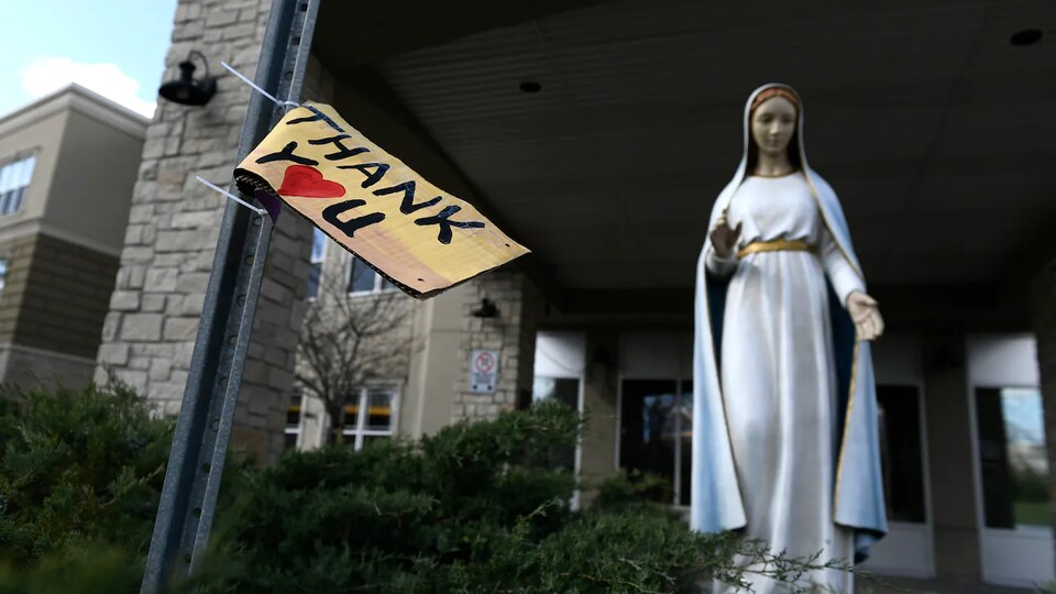 Un message remerciant les travailleurs de la santé à côté d'une statue de Marie à l'extérieur d'une maison de soins.