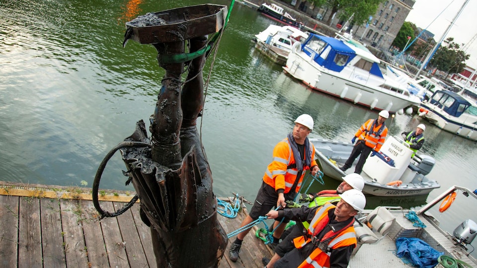 Des travailleurs manipulent une statue suspendue par une grue.