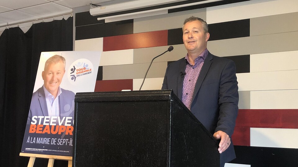 Steeve Beaupré, derrière un lutrin, fait une allocution à côté de sa pancarte électorale pour les élections municipales à Sept-Îles.