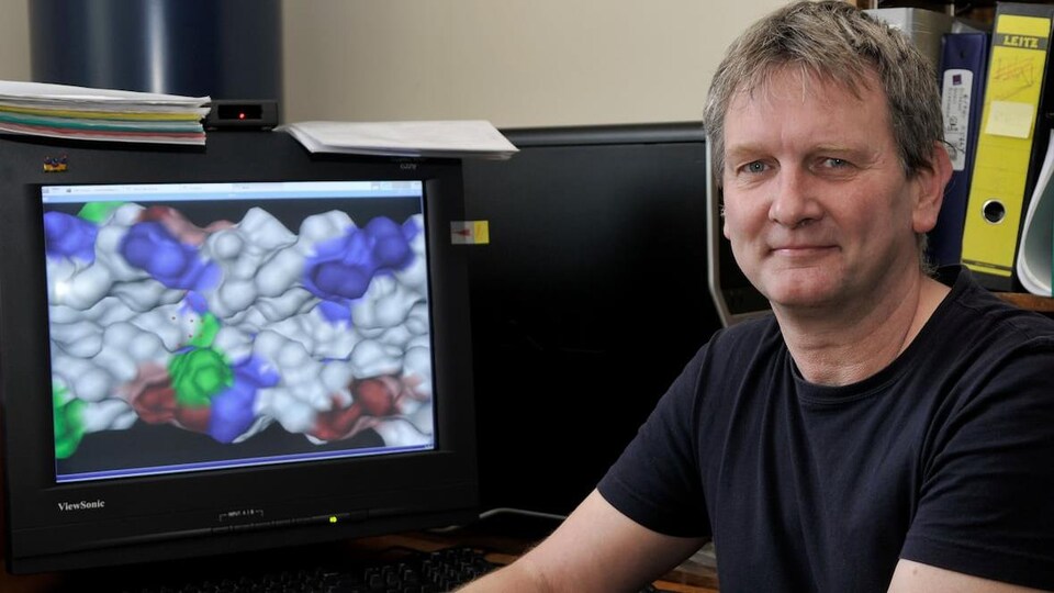 Jörg Stetefeld pose devant un écran qui montre une image prise avec un microscope électronique.