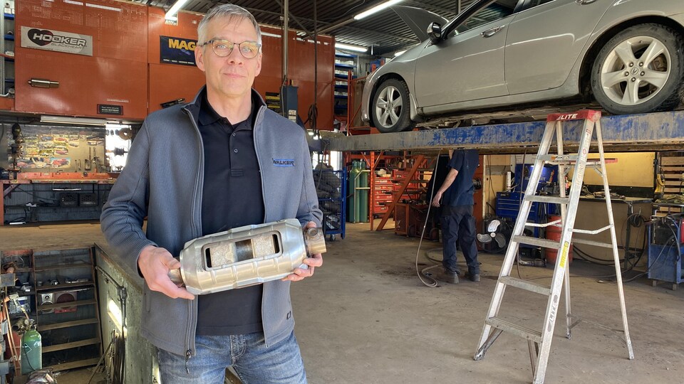 Un homme tient un catalyseur dans ses mains dans un garage.