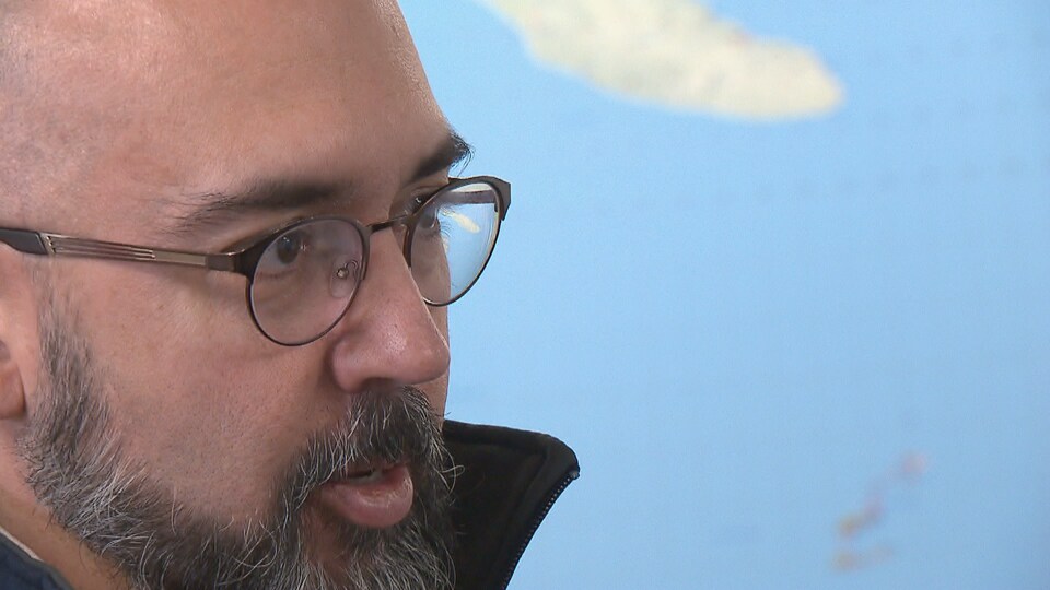 Stéphane Caron appears in front of a map, wearing glasses and a beard.