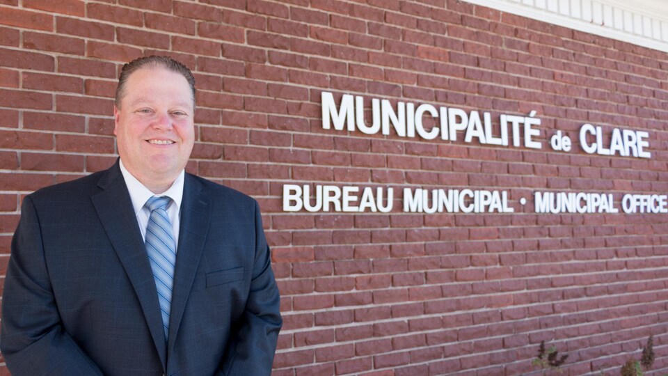 Un homme en complet devant le mur du briques du bureau municipal.