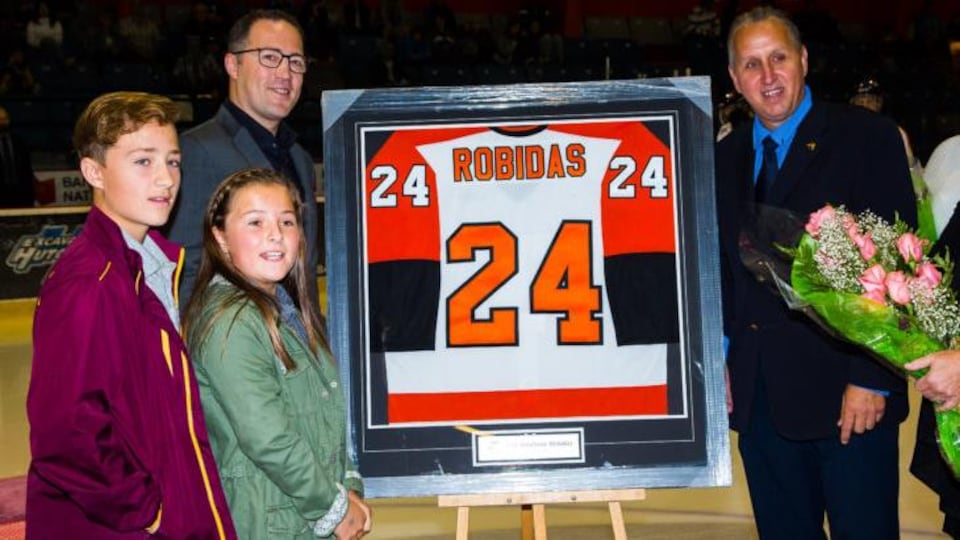 Stéphane Robidas avec ses enfants à côté de son chandail de hockey qui a été retiré.