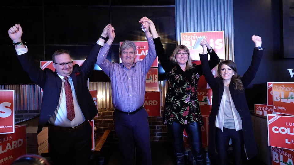 Les candidats libéraux Stephen Blais (à gauche) et Lucille Collard (deuxième en partant de la droite) fêtent leur victoire électorale entourés de John Fraser et Amanda Simard. Ils ont tous les bras en l'air.