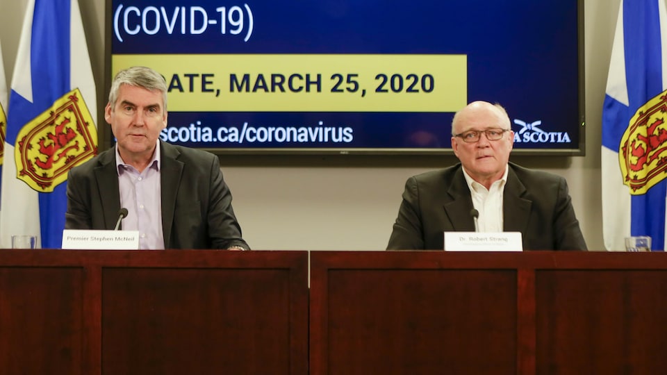 Deux hommes devant un écran géant affichant des informations sur le coronavirus.