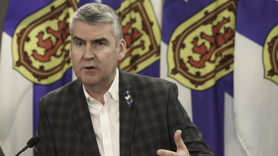 Le politicien s'exprime. En arrière-plan on voit plusieurs drapeaux de la Nouvelle-Écosse. 