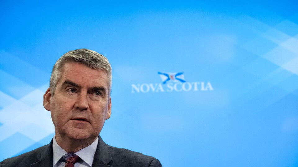Stephen McNeil devant un fond bleu sur lequel est écrit « Nova Scotia » avec un dessin du drapeau de la Nouvelle-Écosse.