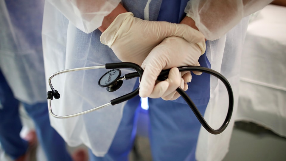 Un médecin les deux mains derrière le dos tient son stéthoscope.