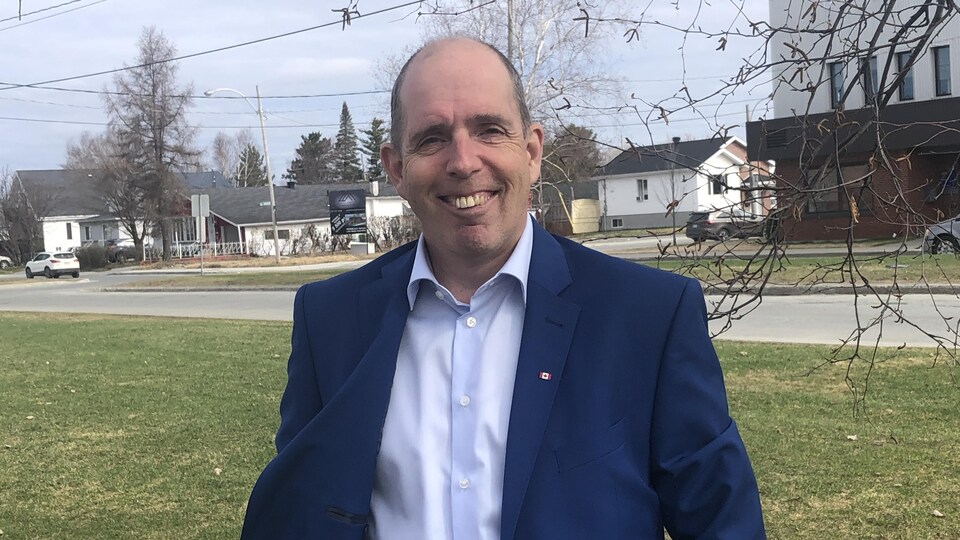 Steve Corriveau, portant un veston avec une épinglette du Canada, sourit dans une rue de Val-d'Or.
