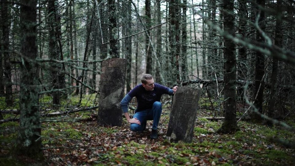 Steve Skafte agenouillé entre deux pierres tombales anciennes au milieu de la forêt.