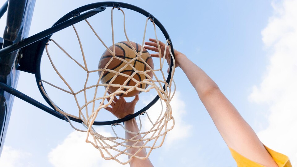 Une personne tient un ballon de basket et le lance dans un panier.