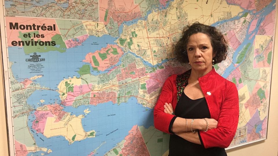 Sue Montgomery devant une carte de la région de Montréal, les bras croisés.