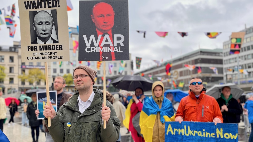 Demonstrators carry placards portraying Russian leader Vladimir Putin as a war criminal.