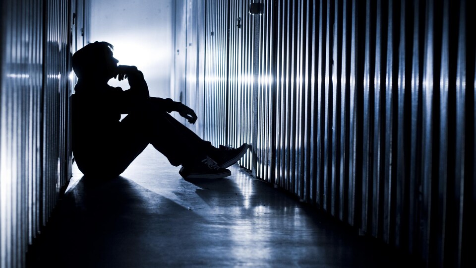 Un adolescent est assis sur le sol dans la pénombre dans un corridor. 