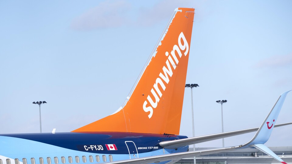 La queue d'un avion au sol peinte en orange avec le mot « Sunwing » en blanc.