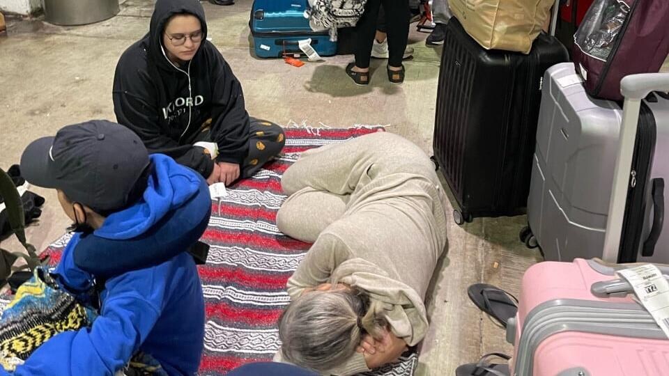 Des gens attendent des autobus avec leurs bagages, certains dorment par terre.