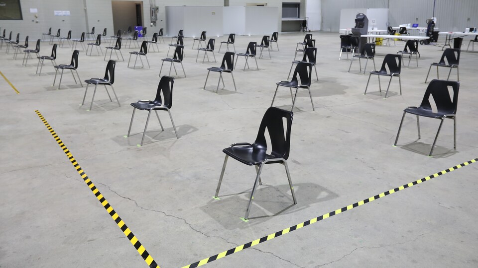 Des chaises disposées à deux mètres de distance dans une grande salle.