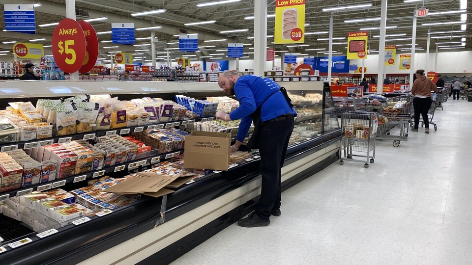 Un homme met des produits dans un rayon de supermarché.