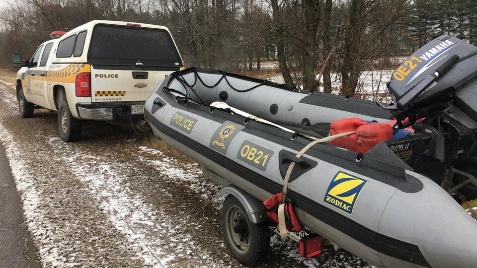Un véhicule de la Sûreté du Québec qui remorque un Zodiac est stationné en bordure d'une route.