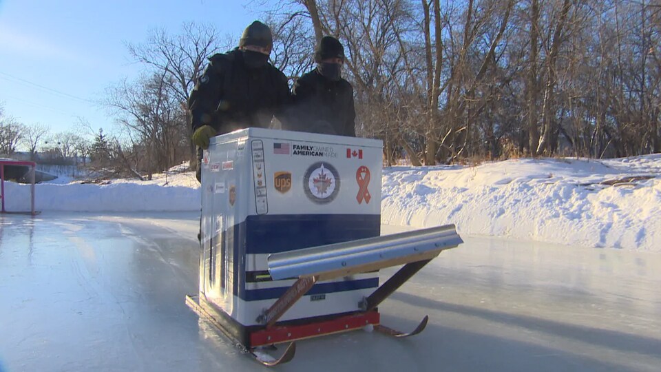 Anthony Theriault et Ron Theriault sont debout derrière la laveuse qui avance sur la patinoire.