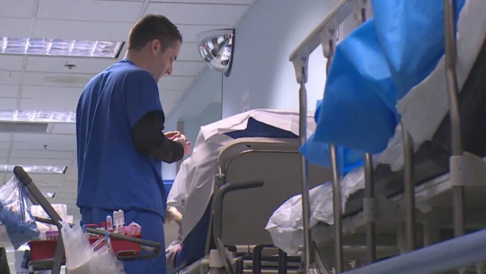 Un infirmier près d'un patient allongé dans un lit se trouvant dans un couloir.