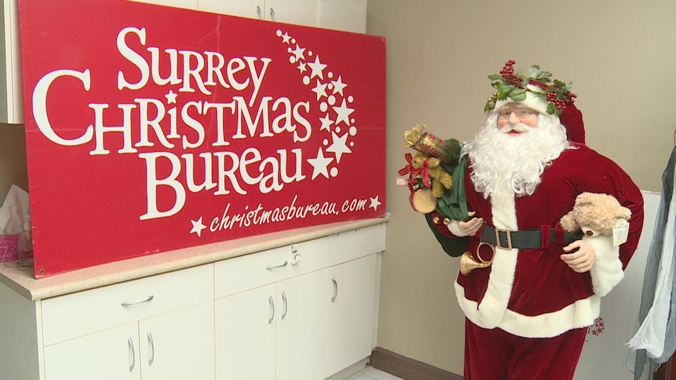 La statue d'un père Noël est debout devant un panneau de l'organisme Surrey Christmas Bureau.