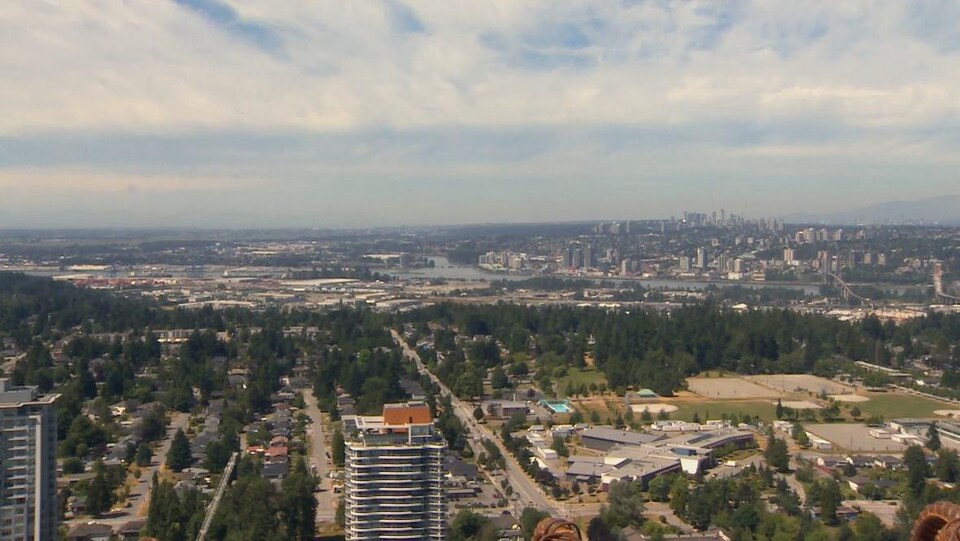 Grand plan de la région de Vancouver pris du haut d'un immeuble de Surrey avec des tours à bureau, une partie du fleuve Fraser et un quartier résidentiel.
