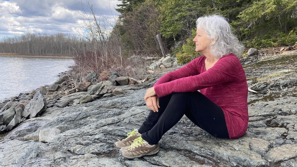 Suzanne Trudel est assise sur un rocher près d'une forêt.